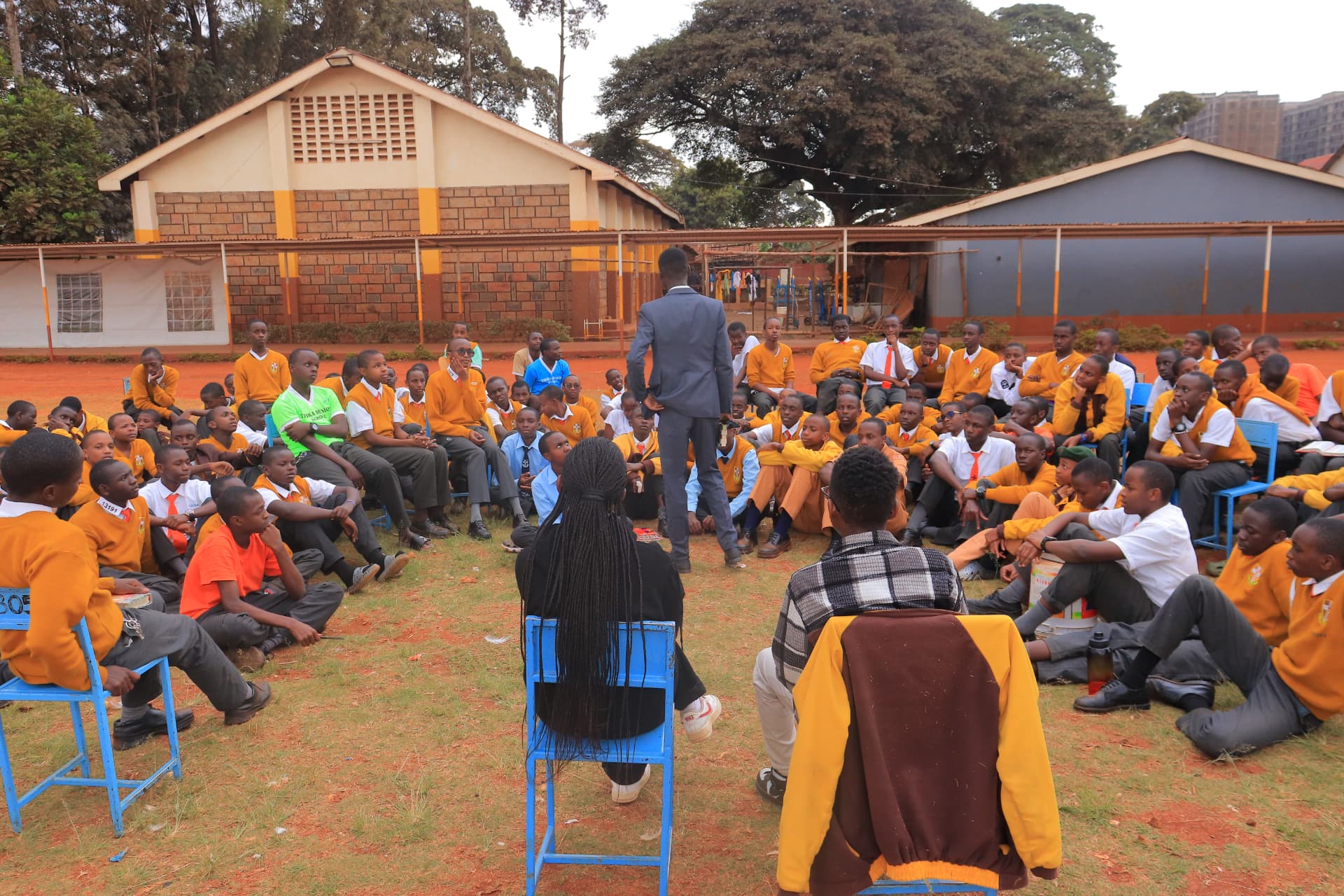 A SET Kenya mentor addressing a circle of students seated outdoors at a school